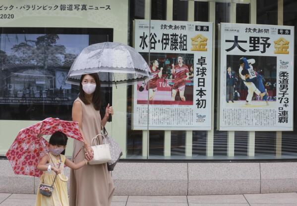 People wearing face masks to protect against the spread of the coronavirus walk past extra papers reporting on Japanese gold medalists at Tokyo Olympics, in Tokyo Tuesday, July 27, 2021. (AP Photo/Koji Sasahara)