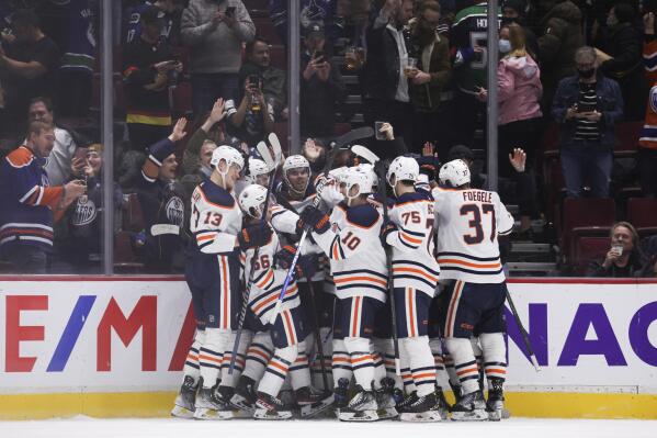 Edmonton Oilers' Connor McDavid, back center, is mobbed by his teammates after scoring the winning goal during overtime in an NHL hockey game, Tuesday, Jan. 25, 2022 in Vancouver, British Columbia. (Darryl Dyck/The Canadian Press via AP)