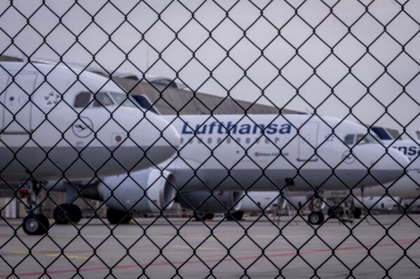 Lufthansa aircrafts are parked behind a fence at the airport in Frankfurt, Germany, Tuesday, March 12, 2024. Many of Germany's train drivers staged a 24-hour strike on Tuesday in the latest installment of a long-running and bitter dispute over working hours with the country's main railway operator, while a walkout by cabin crew at Lufthansa added to disruption for travelers. (AP Photo/Michael Probst)