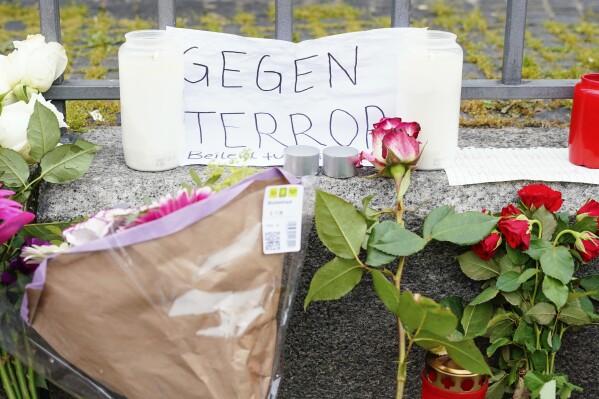 Candles, flowers and a piece of paper with the inscription "Against Terror" stand at the scene of the crime on the market square in Mannheim, Germany, the day after the stabbing at an anti-Islamic rally on Mannheim's market square that injured six people, including a police officer, Saturday, June1, 2024, (Uwe Anspach/dpa via AP)