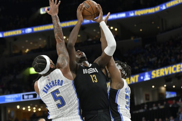 Memphis Grizzlies forward Jaren Jackson Jr. (13) shoots between Orlando Magic forward Paolo Banchero (5) and center Wendell Carter Jr., right, in the first half of an NBA basketball game Friday, Jan. 26, 2024, in Memphis, Tenn. (AP Photo/Brandon Dill)