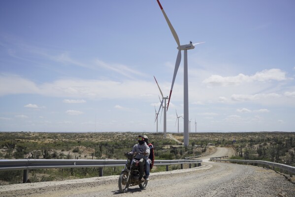 Two people on a motorcycle drive near wind turbines on the outskirts of Cabo de la Vela, Colombia, Feb. 7, 2025. (AP Photo/Ivan Valencia, File)