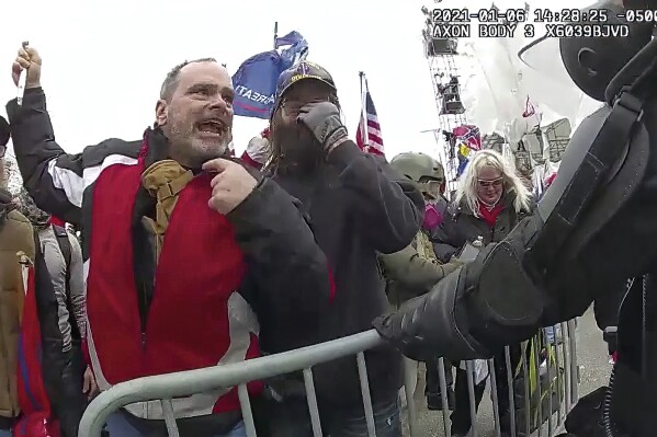 FILE- This still frame from Metropolitan Police Department body worn camera video shows Thomas Webster, in red jacket, at a barricade line at on the west front of the U.S. Capitol on Jan. 6, 2021, in Washington. A federal appeals court has upheld a retired New York Police Department officer’s conviction and 10-year prison sentence for assaulting a police officer during the Jan. 6, 2021, siege at the U.S. Capitol. A three-judge panel from the U.S. Court of Appeals for the District of Columbia Circuit on Tuesday rejected Thomas Webster’s claims that he was convicted by a biased jury. (Metropolitan Police Department via AP)