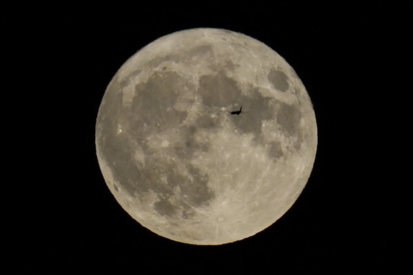 FILE - A plane passes in front of the moon, Aug. 30, 2023, in Chicago. Scientists have confirmed a cave on the moon, not far from where Neil Armstrong and Buzz Aldrin landed 55 years ago this week, and suspect there are hundreds more that could house future astronauts. (AP Photo/Kiichiro Sato, file)