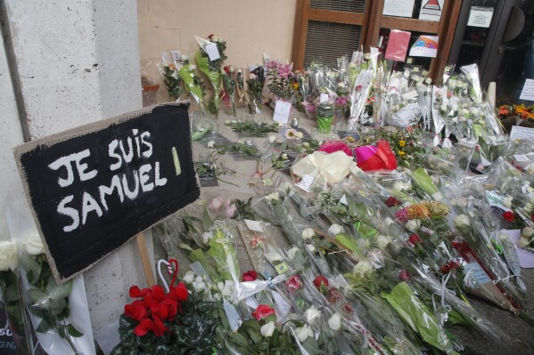 FILE - A poster reading "I am Samuel" and flowers lay outside the school where slain history teacher Samuel Paty was working, Saturday, Oct. 17, 2020 in Conflans-Sainte-Honorine, northwest of Paris. A French juvenile court is handing down a verdict Friday dec.8, 2023 for six teenagers accused of involvement in the killing of teacher Samuel Paty, beheaded by an Islamic extremist after he showed caricatures of the Prophet Muhammad to his class for a debate on freedom of expression. (APPhoto/Michel Euler, File)
