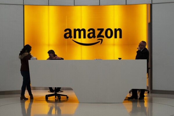 FILE - In this Feb. 14, 2019, file photo, people stand in the lobby for Amazon offices in New York. Amazon is asking some corporate workers to relocate to other cities as part of its return-to-office policy, which mandates workers to be in the office three days a week. (AP Photo/Mark Lennihan, File)