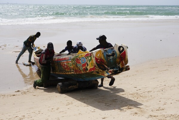 Men push a pirogue on the beach in Saint Louis, Senegal, Sunday, July 16, 2023. Officials and residents say bodies of migrants from capsized boats attempting the dangerous trip from West Africa to Spain are buried in unmarked beach graves. Bodies wash ashore or are found by fishermen at sea, then are buried by authorities. (AP Photo/Sam Mednick)