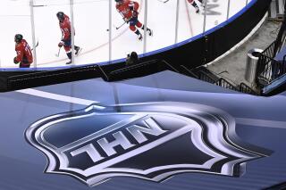 FILE - In this Aug. 14, 2020, file photo, an NHL logo is displayed as Washington Capitals players skate prior to NHL Eastern Conference Stanley Cup playoff hockey game against the New York Islanders in Toronto. The NHL plans to punish unvaccinated players more harshly if they test positive for the coronavirus as part of protocols for the upcoming season. Teams will be able to suspend unvaccinated players without pay if they cannot participate in hockey activities. Those who are fully vaccinated will have any COVID-19 positives treated as hockey injuries and still be paid. (Nathan Denette/The Canadian Press via AP)