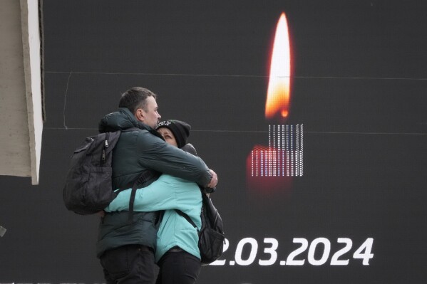 A couple embrace next to a screen with displayed mournful message in St. Petersburg, Russia, Sunday, March 24, 2024. Russia observed a national day of mourning on Sunday, two days after an attack on a suburban Moscow concert hall that killed over 130 people. (AP Photo/Dmitri Lovetsky)