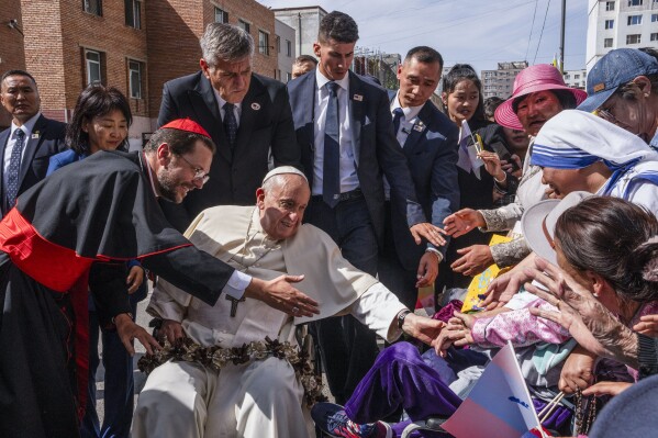 Pope Francis is greeted by Cardinal Giorgio Marengo, left, Apostolic Prefect of Ulaanbaatar, and faithful gathered outside the Apostolic Prefecture in Ulaanbaatar's Kahn Uul district, Friday, Sept. 1, 2023. Pope Francis is traveling to Mongolia to encourage one of the world's smallest and newest Catholic communities. It's the first time a pope has visited the Asian country and comes at a time when the Vatican's relations with Mongolia's two powerful neighbors, Russia and China, are once again strained. (AP Photo/Louise Delmotte)