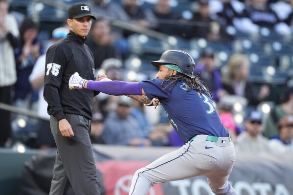 Seattle Mariners' J.P. Crawford, right, celebrates after tripling to drive in three runs as third base umpire Tom Woodring, left, looks on in the second inning of the second game of a baseball doubleheader against the Colorado Rockies, Sunday, April 21, 2024, in Denver. (AP Photo/David Zalubowski)