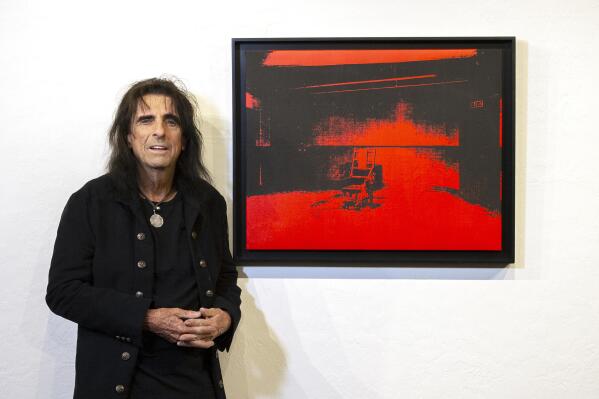 In this photo provided by the Chris Loomis, singer Alice Cooper stands by his Andy Warhol red acrylic and silkscreen on canvas called "Little Electric Chair" at the Larsen Gallery in Scottsdale, Ariz., on Wednesday, May 12, 2021. The Warhol canvas found years ago in the garage of rocker Alice Cooper could become the highest selling artwork ever in Arizona. The music legend, who has a home in metro Phoenix, announced Thursday, May 13, 2021, that he would auction off "Little Electric Chair." The gallery estimates it could fetch anywhere from $2.5 million to $4.5 million. (Chris Loomis via AP)