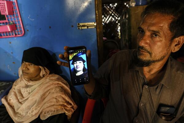 Abdu Shukkur shows a photo of his daughter, Setera Begum, at the Nayapara refugee camp in Teknaf, part of the Cox's Bazar district of Bangladesh, on March 8, 2023. “If you want to go to Malaysia by boat, just divorce your husband,” he told her. “It’s too dangerous.” His wife, Gul Faraz, intervened. “She’s been living without her husband here for 11 years now,” Faraz said. “Let her go.” Shukkur relented. (AP Photo/Mahmud Hossain Opu)