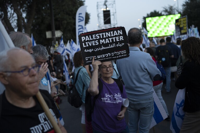 A woman holds up a sign that reads in English 'Palestinians Lives Matter', during a protest against Israeli Prime Minister Benjamin Netanyahu's government and call for the release of hostages held in the Gaza Strip by the Hamas militant group, outside of the Knesset, Israel's parliament, in Jerusalem, Sunday, March 31, 2024. Tens of thousands of Israelis gathered outside the parliament building in Jerusalem on Sunday, calling on the government to reach a deal to free dozens of hostages held by Hamas and to hold early elections. (AP Photo/Leo Correa)