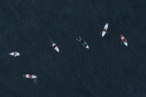 Surfers wait for the perfect wave in Te Aupoo, Tahiti, French Polynesia, Saturday, January 13, 2024.  (AP Photo/Daniel Cole)