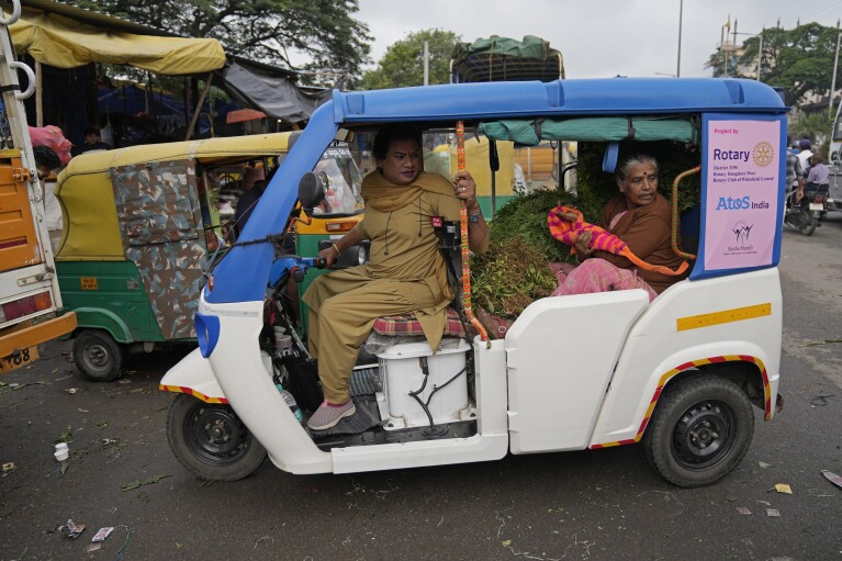 An elderly lady with a load of vegetables travels in an electric auto rickshaw driven by Preethi, a 38-year-old transgender woman who uses only her first name, in Bengaluru, India, Monday, July 10, 2023. (AP Photo/Aijaz Rahi)