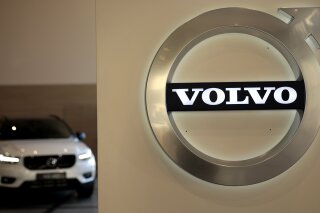 FILE - In this Feb. 6, 2020 file photo a Volvo car is parked behind the Volvo logo in the lobby of the company's corporate headquarters, in Brussels.  Volvo says it will make only electric vehicles by 2030. But for those who want one, they will have to buy it online.  The Swedish automaker said Tuesday, March 2, 2021,  that it is phasing out the production of all cars with internal combustion engines — including hybrids.  (AP Photo/Virginia Mayo, File)