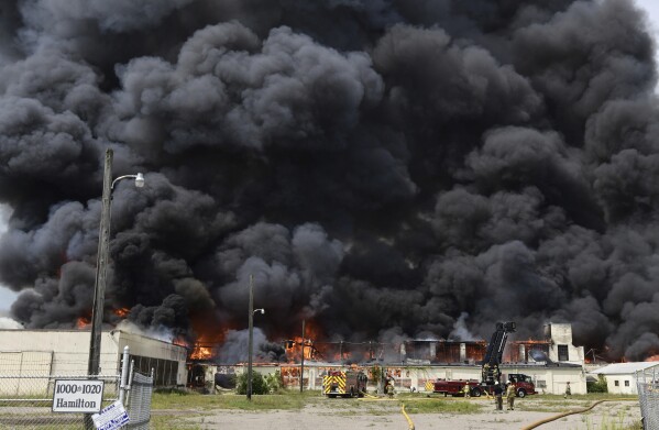 Thick black smoke billows from a blaze as firefighters from multiple departments battle a large fire in commercial buildings along North Street near Hamilton Street in Jackson, Mich., Tuesday, Aug. 22, 2023. (J. Scott Park/Jackson Citizen Patriot via AP)