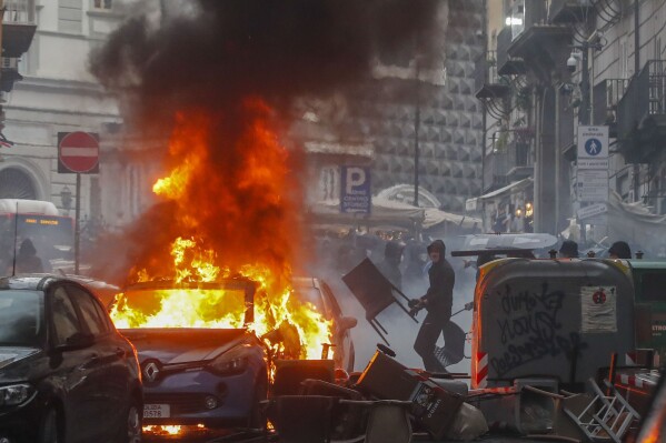 FILE - Supporters of the Eintracht Frankfurt soccer team set a police car afire as they clash with police in Naples, southern Italy, March 15, 2023, where their team is about to play a Champions League, round of 16, second leg soccer match against Naples. A recent surge in violence around soccer games is contributing to alarm over security when Germany hosts the European Championship. Some 22,000 police officers will be on duty each day for the tournament. (AP Photo/Salvatore Laporta, File)