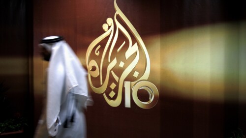 FILE - A Qatari employee of Al-Jazeera Arabic language TV news channel walks past the logo of Al-Jazeera in Doha, Qatar. The pan-Arab news network Al Jazeera has condemned a recent decision by Egyptian authorities to brand some of its journalists as terrorists. The media outlet, which is owned by the Gulf state of Qatar, said that “a number” of its Egyptian journalists and presenters had been added to a list of alleged terrorists published in an official newspaper earlier this month following a ruling by the Cairo Criminal Court. (AP Photo/Kamran Jebreili, File)