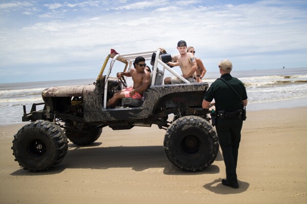 FILE - A group of people riding in a Jeep during the Go Topless Jeep Weekend event get stopped by a Galveston County Sheriff's Office deputy at Crystal Beach on Bolivar Peninsula, Texas, May 17, 2020. (Marie D. De Jesús/Houston Chronicle via AP, File)