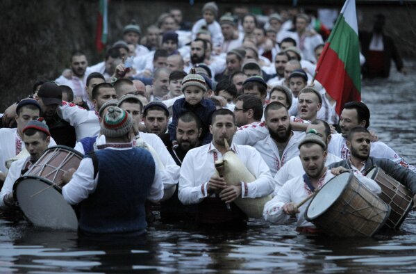 Citizens of the mountain town of Kalofer, in central Bulgaria, clad in traditional dresses stand in the icy Tundzha River, some waving national flags to recover a crucifix cast by a priest in an old ritual marking the feast of Epiphany, Wednesday, Jan. 6, 2021. The legend goes that the person who retrieves the wooden cross will be freed from evil spirits and will be healthy throughout the year. (AP Photo/Valentina Petrova)
