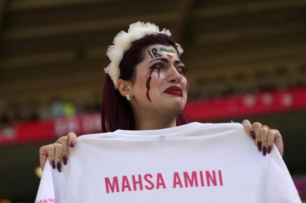 An Iran team supporter cries as she holds a shirt that reads 'Mahsa Amini' prior to the start of the World Cup group B soccer match between Wales and Iran, at the Ahmad Bin Ali Stadium in Al Rayyan, Qatar, Friday, Nov. 25, 2022. (AP Photo/Alessandra Tarantino)