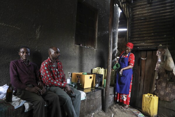 Benson Muhereza, left, an electrical fixer and his friend wait to be served tonto at a local bar in Majengo village in Mbarara, Uganda, Dec. 10, 2023. (AP Photo/Hajarah Nalwadda)