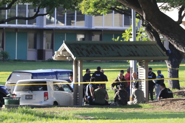 Honolulu police assess the scene around a stolen vehicle stolen on University Avenue, Monday, Jan. 1, 2024, in Honolulu. Authorities in Hawaii say a man shot and wounded a woman, stole a car at gunpoint and was later killed in a shootout with police that left two officers wounded. (Jamm Aquino/Honolulu Star-Advertiser via AP)