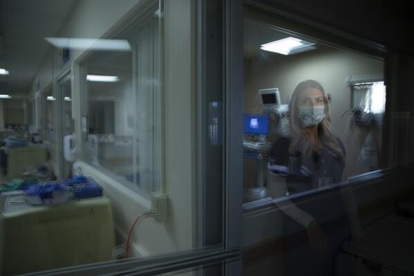 In this photo created with an in-camera multiple exposure, registered nurse Jill Shwam, part of a group of nurses who had been treating coronavirus patients in an intensive care unit, stands for a photo in the empty COVID-19 ICU at Providence Mission Hospital in Mission Viejo, Calif., Tuesday, April 6, 2021. There is a scene that replays in Shwam's head each day: an 11-year-old boy screaming while his mother, in her early 40s, doesn't respond as doctors try to save her. "You need to say goodbye," Shwam remembers saying as the woman's oxygen levels dropped sharply. The woman told her son: "I hope this isn't the last time I talk to you. I have to go." (AP Photo/Jae C. Hong)