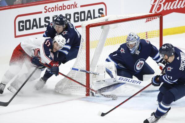 Columbus Blue Jackets' Justin Danforth (17) tries a wraparound on Winnipeg Jets goaltender Eric Comrie (1) as Logan Stanley (64) defends during the second period of an NHL hockey game Friday, March 25, 2022, in Winnipeg, Manitoba. (John Woods/The Canadian Press via AP)