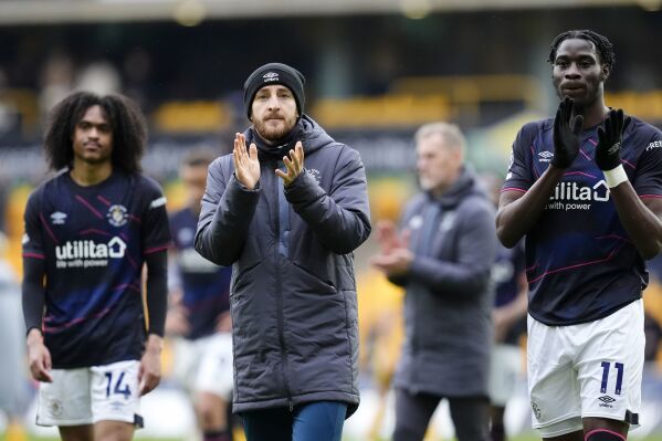 Luton Town's Tom Lockyer, centre, and team-mate Elijah Adebayo applaud the fans following the Premier League match between Wolverhampton Wanderers and Luton Town at Molineux Stadium, Wolverhampton, England, Saturday April 27, 2024. Tom Lockyer, the Premier League player who suffered an onfield cardiac arrest earlier this season, says he is “at peace” if he is forced to retired from the sport. (Nick Potts/PA via AP)