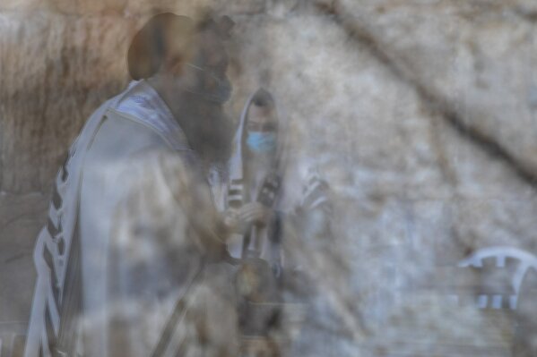Ultra-Orthodox Jewish men wearing face masks, are reflected on a door window, as they pray ahead of Yom Kippur, the holiest day in the Jewish year which starts at sundown Sunday during a three-week nationwide lockdown to curb the spread of the coronavirus at the Western Wall, the holiest site where Jews can pray in Jerusalem's old city, Sunday, Sept. 27, 2020. (AP Photo/Ariel Schalit)