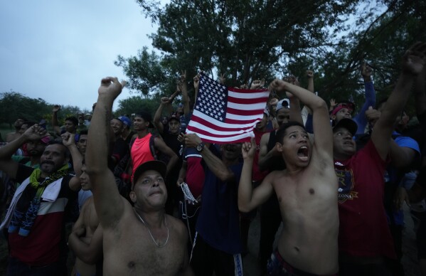 Venezuelan migrants wave a U.S. flag at a television helicopter flying over the Rio Grande in Matamoros, Mexico, on May 12, 2023, a day after pandemic-related asylum restrictions called Title 42 were lifted. (AP Photo/Fernando Llano)
