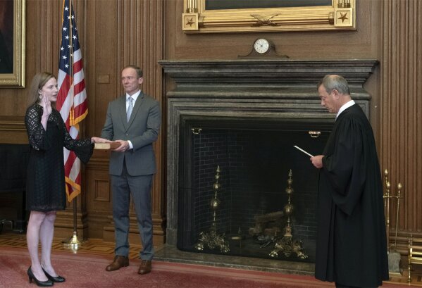 In this image provided by the Collection of the Supreme Court of the United States, Chief Justice John G. Roberts, Jr., right, administers the Judicial Oath to Judge Amy Coney Barrett in the East Conference Room of the Supreme Court Building, Tuesday, Oct. 27, 2020, in Washington as Judge Barrett's husband, Jesse M. Barrett, holds the Bible. (Fred Schilling/Collection of the Supreme Court of the United States via AP)