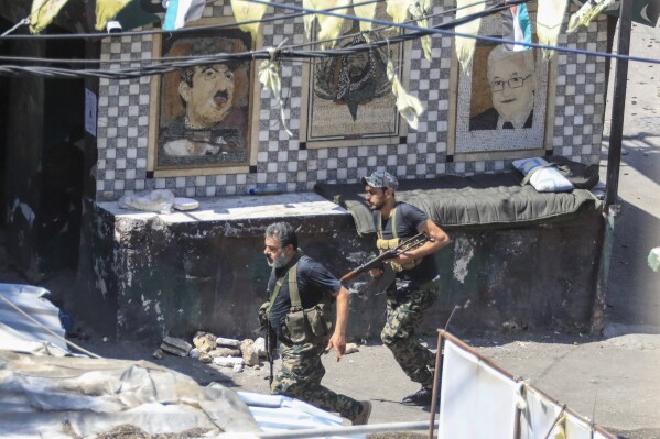 FILE - Members of the Palestinian Fatah group run to take position during a third day of clashes that erupted with Islamist factions in the Palestinian refugee camp of Ein el-Hilweh near the southern port city of Sidon, Lebanon, on July 31, 2023. Damages to the school complex in Lebanon's largest Palestinian refugee camp from clashes that erupted between factions in the camp over the past week could delay the start of the school year for some 6,000 children, the Lebanon head of the UN agency for Palestinian refugees said Friday, Aug. 4. (AP Photo/Mohammad Zaatari, File)