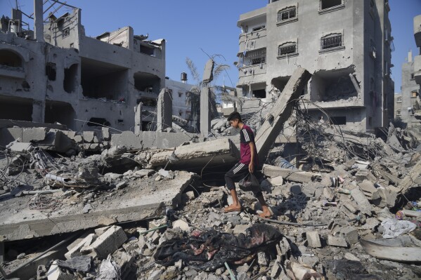Des Palestiniens se tiennent à côté du bâtiment détruit lors d’une frappe aérienne israélienne à Deir al-Balah, dans le sud de la bande de Gaza, le samedi 14 octobre 2023. (AP Photo/Hatem Moussa)