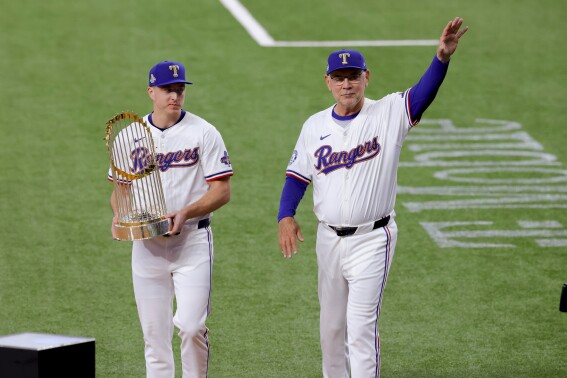 Texas Rangers relief pitcher Josh Sborz, left, and manager Bruce Bochy, right, walk the Commissioner's Trophy onto the field before the team's baseball game against the Chicago Cubs, Thursday, March 28, 2024 in Arlington, Texas. (AP Photo/Gareth Patterson)