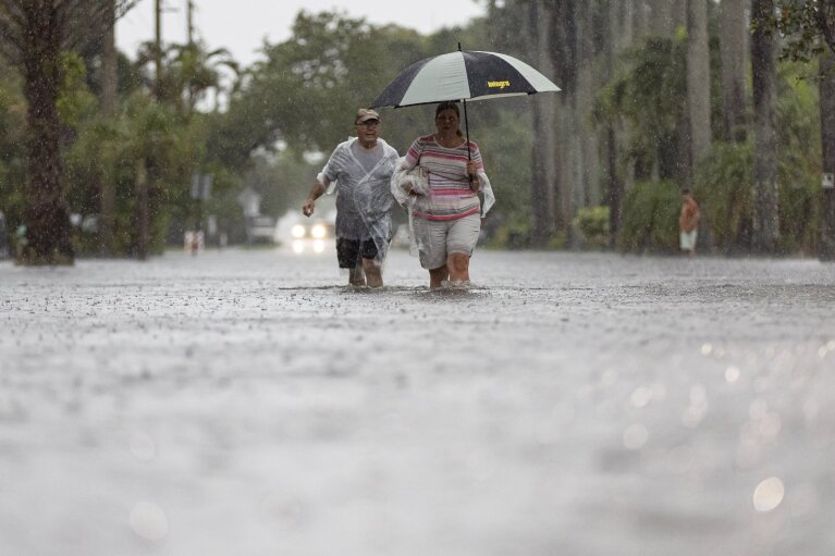 2024년 6월 12일 수요일, 플로리다주 할리우드  (Matthias J. Ochner/Miami Herald via AP) Jim Comunale과 Pam Mervos가 2024년 6월 12일 인근 지역에 폭우가 쏟아지는 가운데 Arthur Street를 걷고 있습니다.