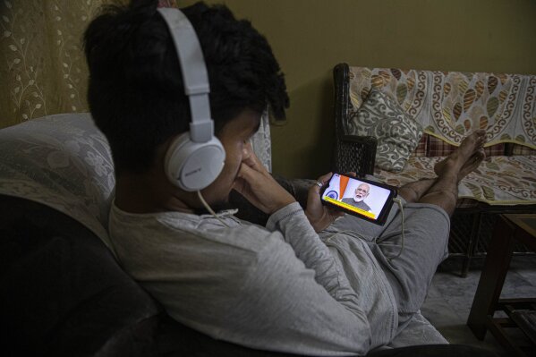 An Indian boy watches Prime Minister Narendra Modi address the nation in a televised speech about COVID-19 situation, on his mobile phone in Gauhati, India, Tuesday, March 24, 2020. Modi Tuesday announced a total lockdown of the country of 1.3 billion people to contain the new coronavirus outbreak. For most people, the new coronavirus causes only mild or moderate symptoms. For some it can cause more severe illness. (AP Photo/Anupam Nath)