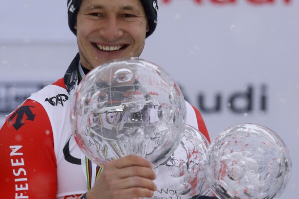 Switzerland's Marco Odermatt holds the alpine ski World Cup overall title trophy, left, and the trophies for downhill, super-G and giant slalom disciplines as he celebrates on the podium, in Saalbach, Austria, Sunday, March 24, 2024. (AP Photo/Alessandro Trovati)