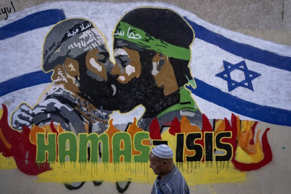 FILE - A man walks past a newly painted graffiti that reads Hamas equal ISIS, in Tel Aviv, Israel, Monday, Oct. 30, 2023. It has become an Israeli mantra throughout the latest war in Gaza: Hamas is ISIS. Since the bloody Hamas attack on Oct. 7 that triggered the war, Israeli leaders and commanders have likened the Palestinian militant group to the Islamic State group. They point to Hamas’ brutal slaughter of hundreds of civilians and compare their Gaza war to the U.S.-led campaign to defeat IS in Iraq and Syria. (AP Photo/Oded Balilty, File)