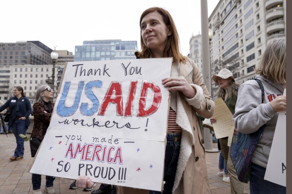 A person carries a sign in support of the United States Agency for International Development (USAID) workers, as they carry their personal belongings after retrieving them from the USAID's headquarters in Washington, Feb. 27, 2025. (AP Photo/Jose Luis Magana, File)