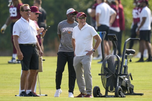 Washington Commanders owner Josh Harris, right, laughs with Joe Theismann, left, Mitchell Rales, and others, during NFL football practice at the team's training facility, Wednesday, July 26, 2023 in Ashburn, Va. (AP Photo/Alex Brandon)