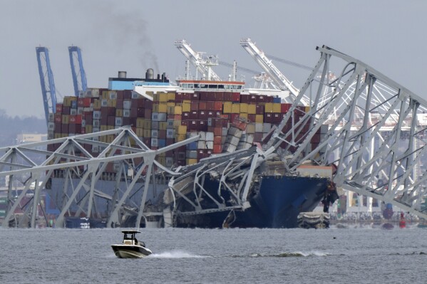 Un barco pasa frente a un buque portacontenedores que chocó contra el puente Francis Scott Key, el martes 26 de marzo de 2024, en Baltimore, Maryland. (Foto AP/Mark Schiefelbein)