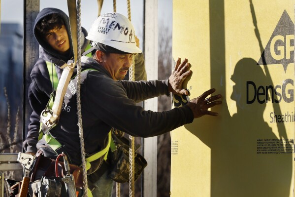 Workers apply sheathing to the exterior of a new multifamily residential building, Friday, Nov. 3, 2023, in the East Boston neighborhood of Boston. According to a raft of polls and surveys, most Americans hold a glum view of the economy. (AP Photo/Michael Dwyer)
