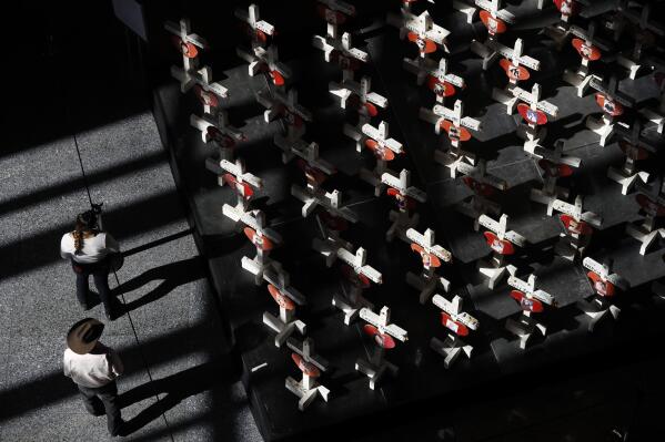FILE - In this Sept. 25, 2018, photo, people look at a display of wooden crosses and a Star of David on display at the Clark County Government Center in Las Vegas. It was the deadliest mass shooting in modern U.S. history on the Las Vegas Strip in 2017. More than 100 people have been killed in mass shootings thus far in 2023, an average of one mass killing a week. (AP Photo/John Locher, File)