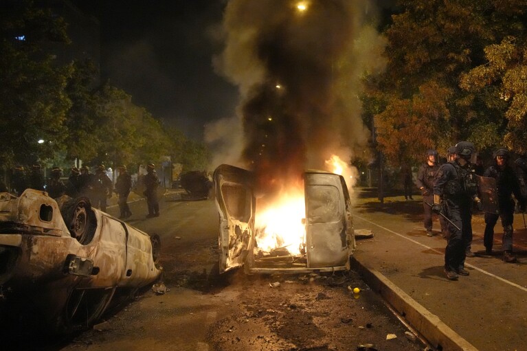 Police forces walk past burning cars in Nanterre, outside Paris, Thursday, June 29, 2023. The death of 17-year-old Nael by police during a traffic check Tuesday in the Paris suburb of Nanterre elicited nationwide concern and widespread messages of indignation and condolences. Interior Minister Gerald Darmanin said 1,200 police were deployed overnight and 2,000 would be out in force Wednesday in the Paris region and around other big cities to "maintain order."(AP Photo/Christophe Ena)