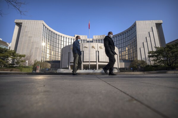 FILE - Pedestrians wearing face masks walk past the People's Bank of China in Beijing on March 3, 2023. China’s central bank said Wednesday, Jan. 24, 2024, it will cut the ratio of reserves banks must hold to help boost the slowing economy. (AP Photo/Mark Schiefelbein, File)