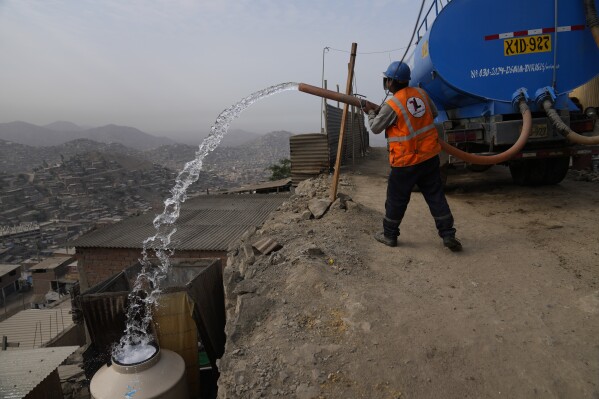 A water truck worker fills a container outside the homes of residents who use it for drinking, cooking and cleaning, in the Pamplona Alta area in Lima, Peru, Friday, March 8, 2024. (AP Photo/Martin Mejia)